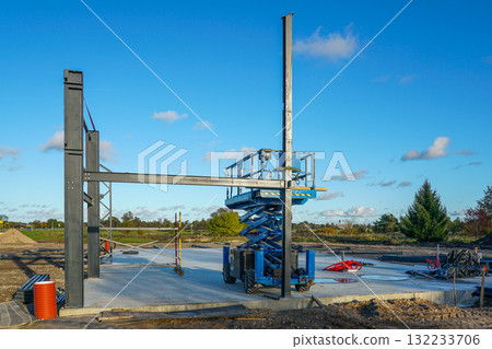 Steel frame structure under construction with scissor lift on building site against blue sky 132233706