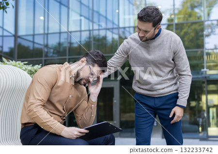 Male colleagues show empathy and support each other during career stress or professional frustration, offering comfort and understanding in an outdoor business setting 132233742