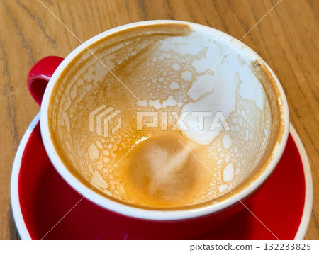 Empty coffee cup with foam traces on red saucer. Warmth, everyday ritual and comfort after morning drink in cozy cafe. Empty coffee cup with foam traces on red saucer. Warmth, everyday ritual and comfort after morning drink in cozy cafe. 132233825