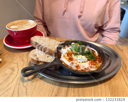 Breakfast with shakshuka, bread and cappuccino on wooden table. Food and Mediterranean flavors in cozy cafe setting. 132233829
