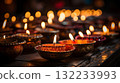 A close up Diya oil lamps in small bowls with red flowers on dark background. Warm and inviting Diwali mood 132233993