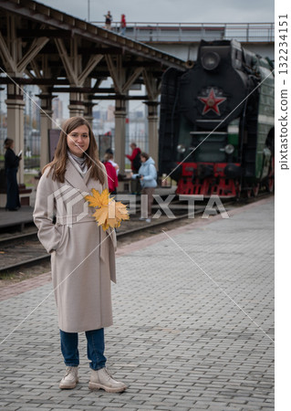 Woman with autumn leaves on her shoulder stands near an old steam locomotive at a railway station in Moscow Woman with autumn leaves on her shoulder stands near an old steam locomotive at a railway station in Moscow 132234151