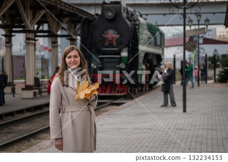 Woman with autumn leaves on her shoulder stands near an old steam locomotive at a railway station in Moscow Woman with autumn leaves on her shoulder stands near an old steam locomotive at a railway station in Moscow 132234153