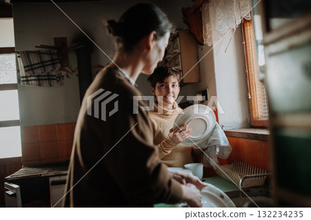 Girl helping mother to wash dishes in an old rural kitchen. 132234235