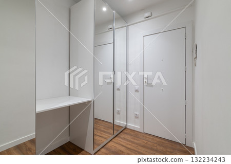 A modern hallway with a large mirror and a white door. The floor is wooden, and the walls are painted white, creating a bright and spacious atmosphere. 132234243