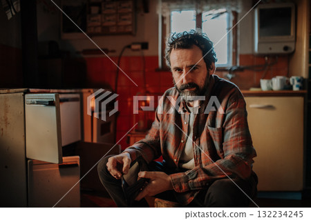 Despaired man sitting by wood stove in aged interior. Despaired man sitting by wood stove in aged interior. 132234245