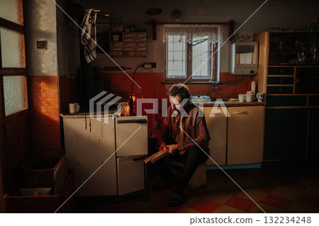 Despaired man sitting by wood stove in aged interior. 132234248