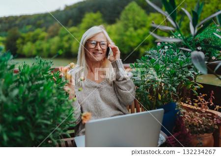 Mature woman sitting on balcony making phone call, working remotely. 132234267