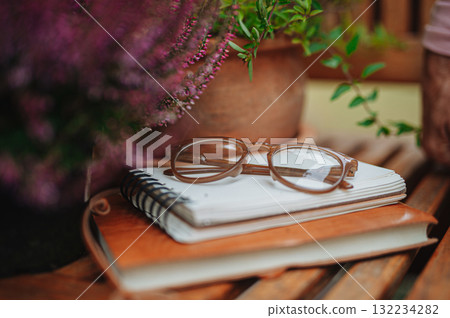 Reading glasses resting on notebook in autumn garden Reading glasses resting on notebook in autumn garden 132234282