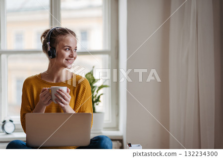 Young female student with headphones sitting at the table and studying. 132234300