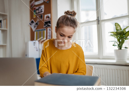 Young female student sitting at the table and studying. 132234306