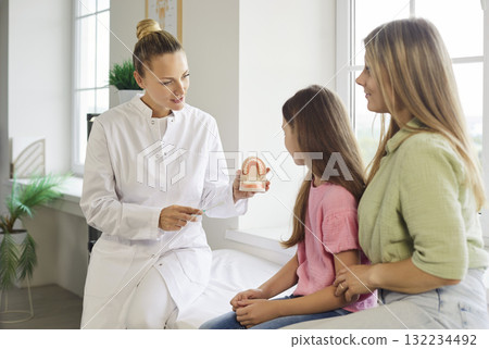 Dentist teaching child and mother tooth brushing with model during pediatric visit 132234492