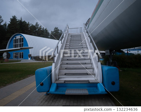 boarding stairs beside parked airplane under clouds, passenger boarding at aircraft stairs beneath overcast sky, scene of passengers ascending boarding stairs beside grounded aircraft boarding stairs beside parked airplane under clouds, passenger boarding at aircraft stairs beneath overcast sky, scene of passengers ascending boarding stairs beside grounded aircraft 132234636