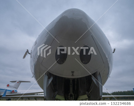 close frontal shot of passenger jet nose resembling smile, cockpit windows and painted markings create character, polished metal surface reflects cloudy sky, static display on grassy field 132234686