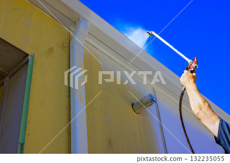 Worker is spraying building exterior with water to keep it clean and maintained. 132235055