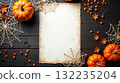 Halloween pumpkins, berries, and cobwebs arranged around aged paper on black wooden table, festive autumn holiday background concept Space for text 132235204