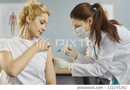 Masked doctor administering vaccine injection to adult patient in bright clinic 132235262