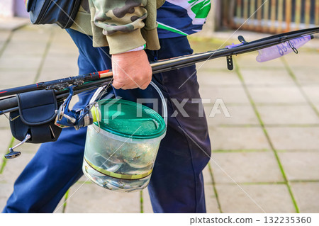 Close-up of fisherman holding fishing rods and bucket full of fresh catch walking on paved city street. Concept of fishing, outdoor hobby, fresh seafood Close-up of fisherman holding fishing rods and bucket full of fresh catch walking on paved city street. Concept of fishing, outdoor hobby, fresh seafood 132235360