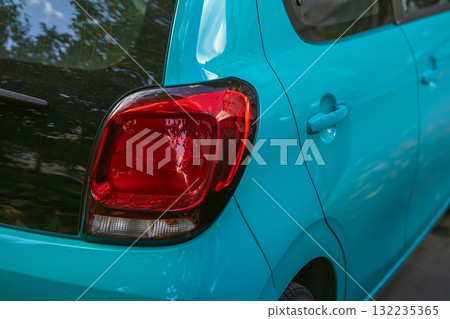 Close-up of turquoise compact car rear with red tail light and shiny reflections. Concept of modern design, urban transportation, automobile detail, vibrant city lifestyle Close-up of turquoise compact car rear with red tail light and shiny reflections. Concept of modern design, urban transportation, automobile detail, vibrant city lifestyle 132235365