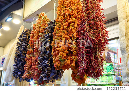 Colorful display of dried vegetables hanging in a market, offering a vibrant assortment of produce. Colorful display of dried vegetables hanging in a market, offering a vibrant assortment of produce. 132235711