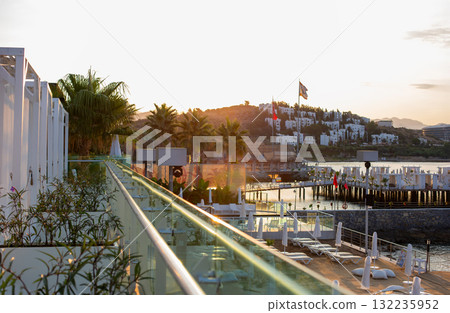 Wooden Pier with White Loungers Over the Sea Turkey. Well-designed wooden pier extends into calm sea, with white loungers and national flags, evoking peaceful holiday setting. 132235952