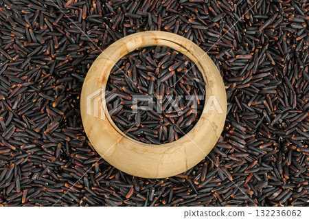 Black rice in a wooden bowl as a background. Top view. Flat lay 132236062