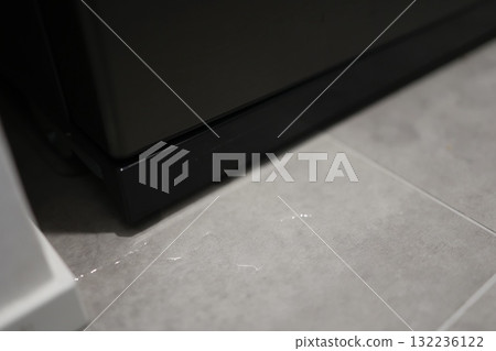 The floor appears to be wet due to a water leak from the bottom of the refrigerator (freezer). 132236122