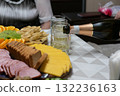 Close-up of a festive table with sliced cheese, sausage, fruits, and biscuits as champagne is poured into a glass. Celebration scene filled with warmth, delicious food, and joyful atmosphere 132236163