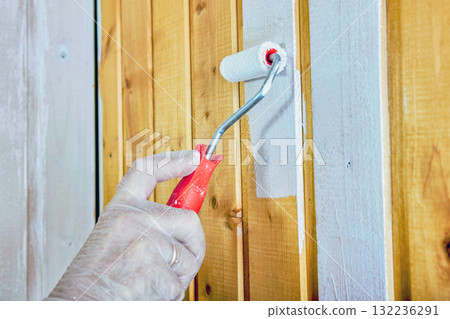 Construction worker uses roller to evenly coat wooden panels with white paint. 132236291