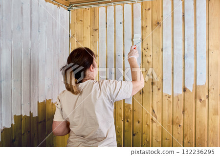 Worker rolls white paint onto vertical wooden planks. 132236295