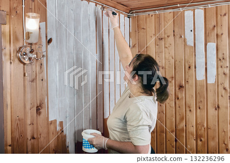 Interior painting of room with tongue and groove paneling walls painted white house painter uses paintbrush to paint joints. 132236296