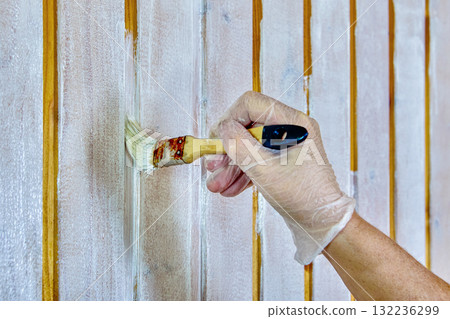 House painter uses paintbrush to paint joints of clapboard during wall painting. 132236299