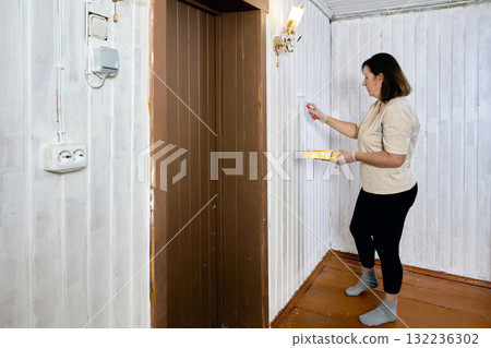 Need to refresh appearance of tongue and groove walls seems to have arisen, painter uses roller to cover old panels with first layer of white paint near corner. 132236302