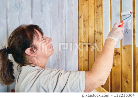 Painter applies white paint using roller on wooden slats. 132236304