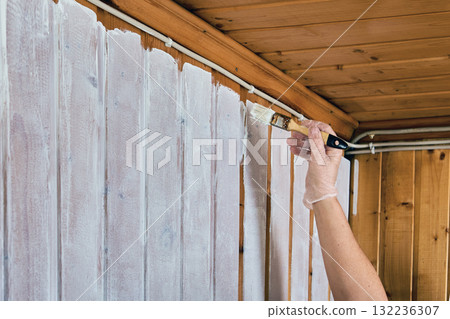 During painting of room with wooden paneling house painter uses paintbrush to apply white paint to joints. During painting of room with wooden paneling house painter uses paintbrush to apply white paint to joints. 132236307