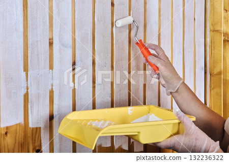 Painting tongue and groove paneling white color house painter uses small paint roller dipping paint in tray. 132236322