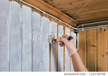 Small paintbrush helps paint joints of wooden paneling when applying white paint to walls. 132236346