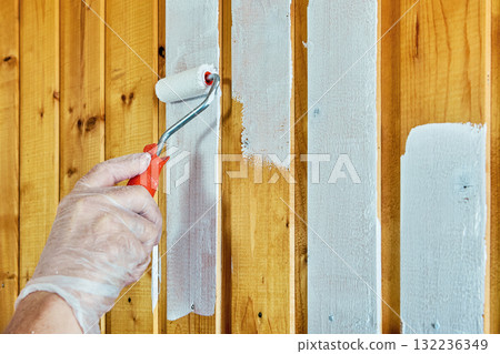 House painter applies white paint with roller on wooden panels. House painter applies white paint with roller on wooden panels. 132236349
