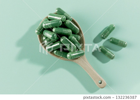 Green spirulina capsules in spoon on mint background. Organic superfood supplement for health, detox immunity support. 132236387