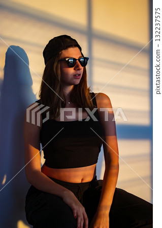Teen girl wearing a trendy cap, rapper style, posing under the soft golden light of sunset. 132237575