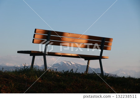 A wooden bench is sitting on a grassy hillside A wooden bench is sitting on a grassy hillside 132238511
