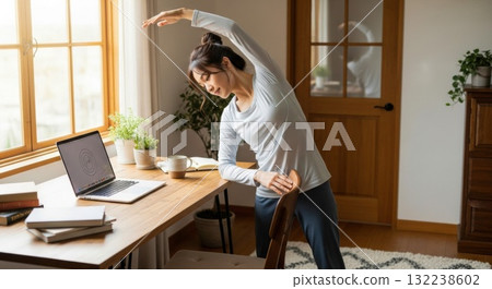 A woman working from home stretching next to her desk 132238602