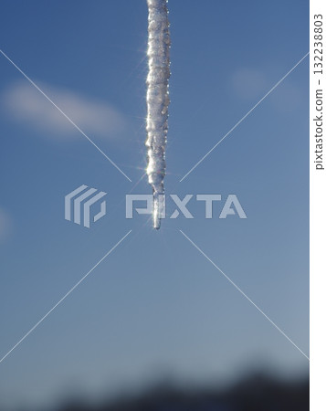 A long icicle hanging from a tree branch A long icicle hanging from a tree branch 132238803