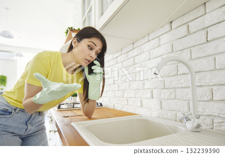 Woman in kitchen calling plumber to fix clogged sink drain at home 132239390