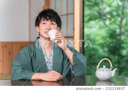 身穿浴衣的亞洲年輕男子在日式旅館的房間喝茶 身穿浴衣的亞洲年輕男子在日式旅館的房間喝茶 132239837