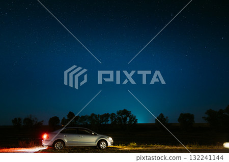 Car Sedan Parking On A Roadside Of Country Road On A Background Of Blue Sky At Winter Season. Country Asphalt Road In Countryside. Night View Of Natural Glowing Stars. Ground In Lights From Rear Red Car Sedan Parking On A Roadside Of Country Road On A Background Of Blue Sky At Winter Season. Country Asphalt Road In Countryside. Night View Of Natural Glowing Stars. Ground In Lights From Rear Red 132241144
