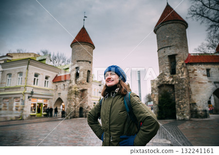 Tallinn, Estonia. Young Caucasian Girl Woman Backpacker Enjoying And Smiling Near Famous Landmark Viru Gate. Vacation In Old Town Tallinn, Estonia. Young Caucasian Girl Woman Backpacker Enjoying And Smiling Near Famous Landmark Viru Gate. Vacation In Old Town 132241161