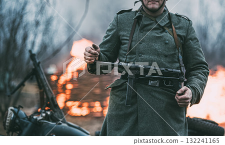 German Wehrmacht Infantry Soldier In World War Ii Standing Against The Background Of A Burning House. German WWII Soldier German Wehrmacht Infantry Soldier In World War Ii Standing Against The Background Of A Burning House. German WWII Soldier 132241165