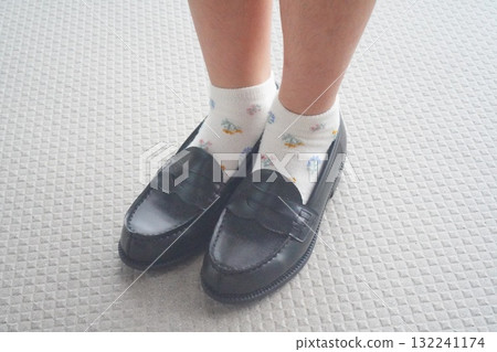 A photo of feet wearing white socks with a small floral pattern and black loafers. The composition exudes cuteness and cleanliness. 132241174
