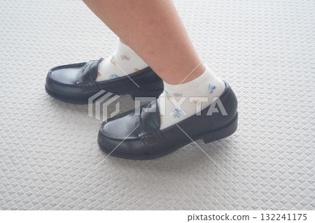 This photo shows her feet in black loafers, taken from an angle. The natural, standing pose, enveloped in soft light, is striking. This photo shows her feet in black loafers, taken from an angle. The natural, standing pose, enveloped in soft light, is striking. 132241175